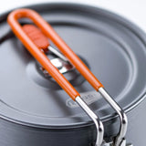 Close-up of a dark gray cookware lid with an orange silicone handle and silver metal clips, photographed on a clean white background.